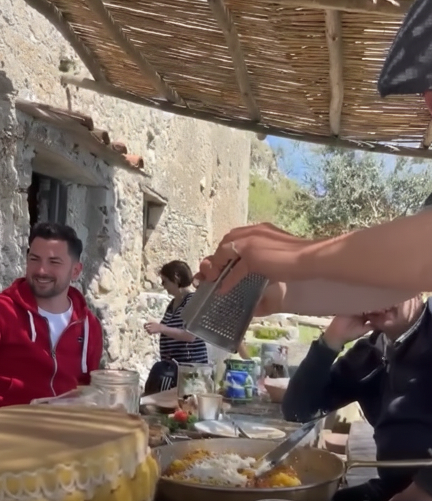 Two men enjoying an outdoor cooking class on a terrace overlooking the colorful houses of Positano and the Amalfi Coast.