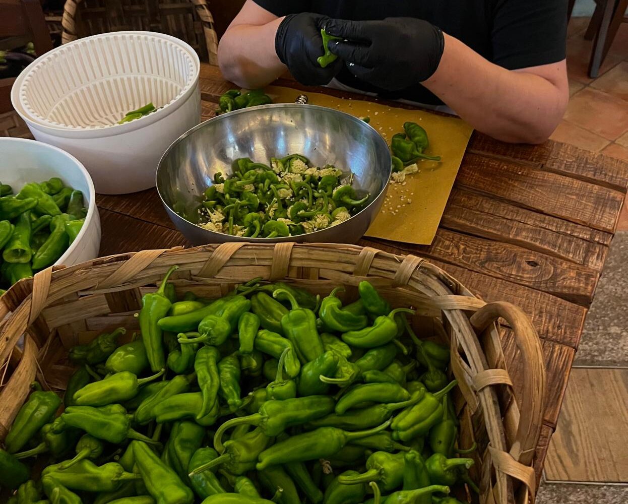 Local woman preparing fresh green Italian peppers (friggitelli) in a rustic farm kitchen.