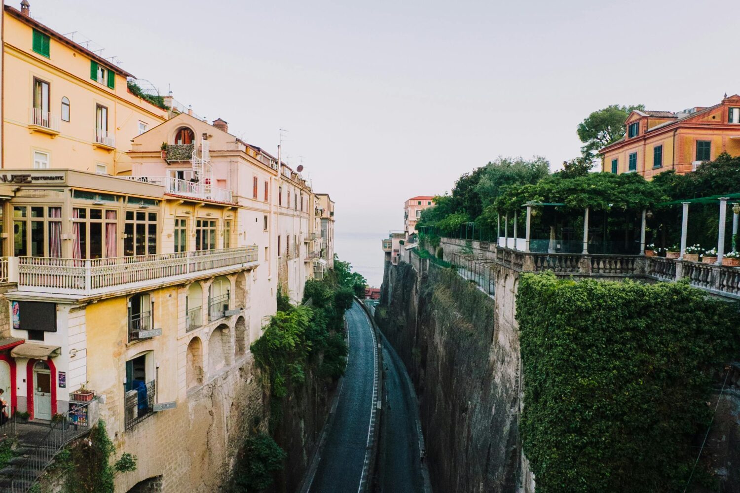 Deep valley road in Sorrento with historic buildings and lush green cliffs under a clear sky.