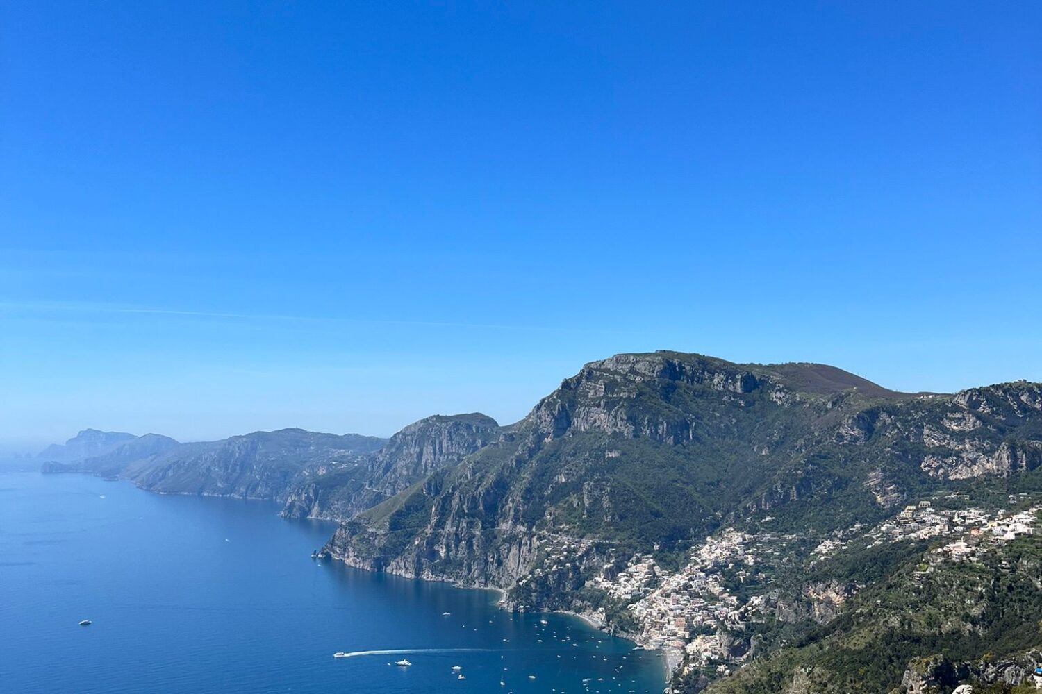 High angle aerial view of the Amalfi Coast coastline with blue sea, mountains, and the Path of the Gods hiking trail.