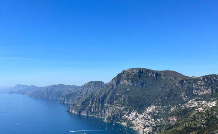 High angle aerial view of the Amalfi Coast coastline with blue sea, mountains, and the Path of the Gods hiking trail.